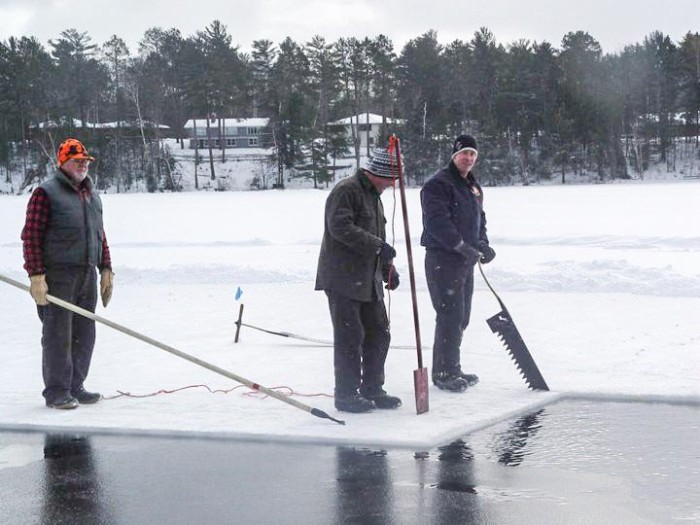Three men standing on a frozen pond with shovels.