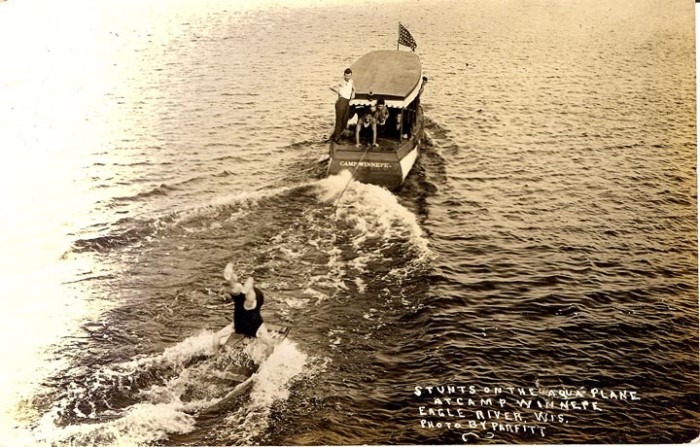 A man is swimming in the water with a boat behind him.