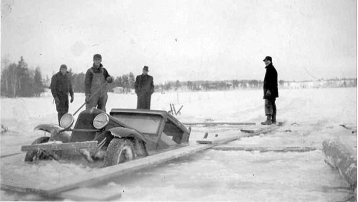 A group of men standing next to a car in the snow.