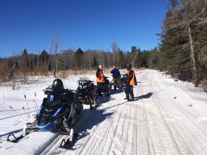 A group of people on snowmobiles on a snowy trail.