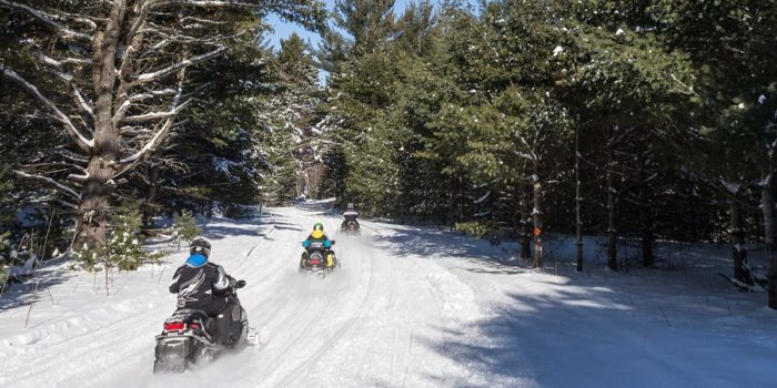 A group of people riding snowmobiles down a snowy trail.
