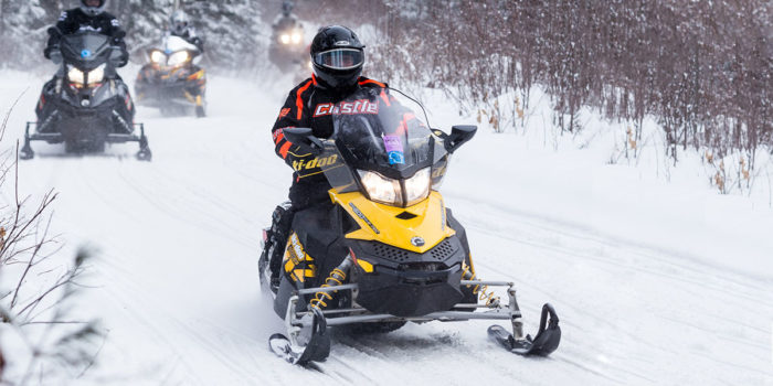 A group of people riding snowmobiles down a snowy trail.