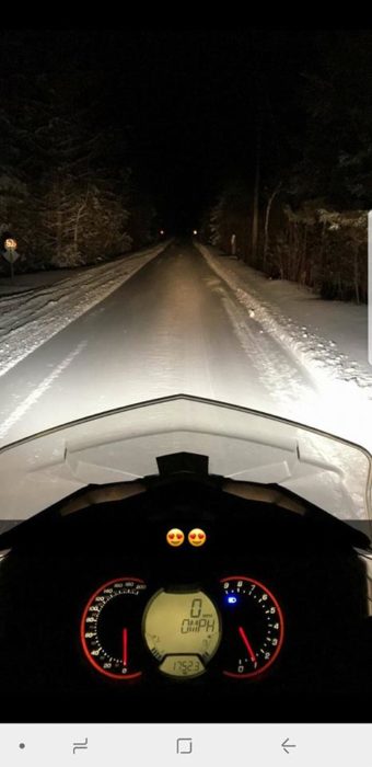 A motorcycle driving down a snowy road with lights on.
