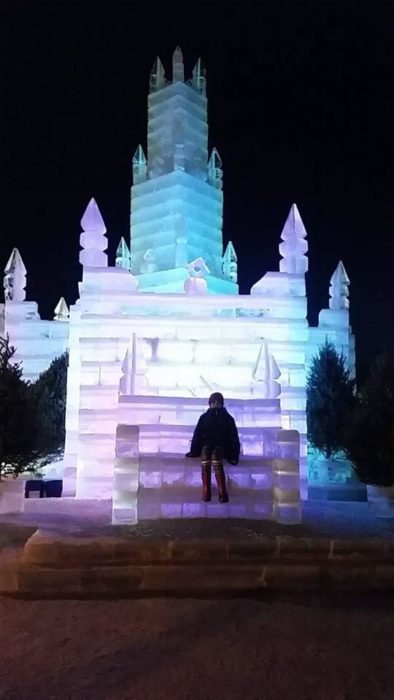 A person sitting in front of an ice castle at night.