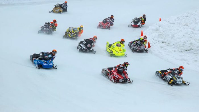 A group of people riding snowmobiles down a snowy hill.