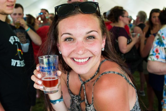 A woman holding a glass of beer at a festival.