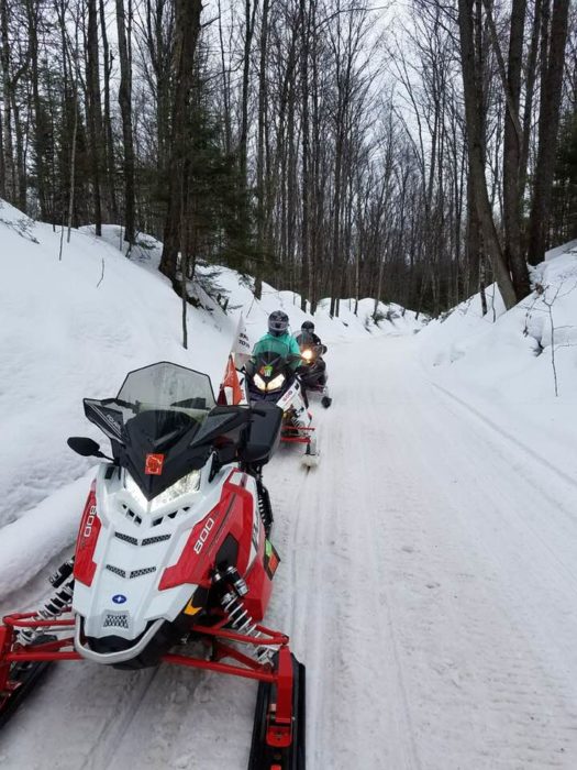 A group of people riding snowmobiles down a snowy road.