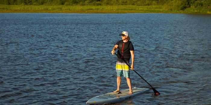 A man standing on a paddle board in a body of water.