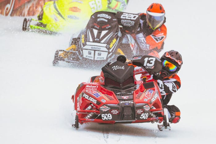 A group of snowmobile racers racing down a snowy hill.