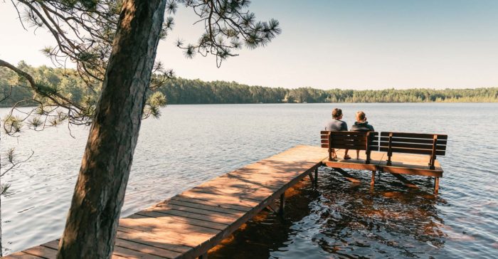 Two people sitting on a dock overlooking a lake.