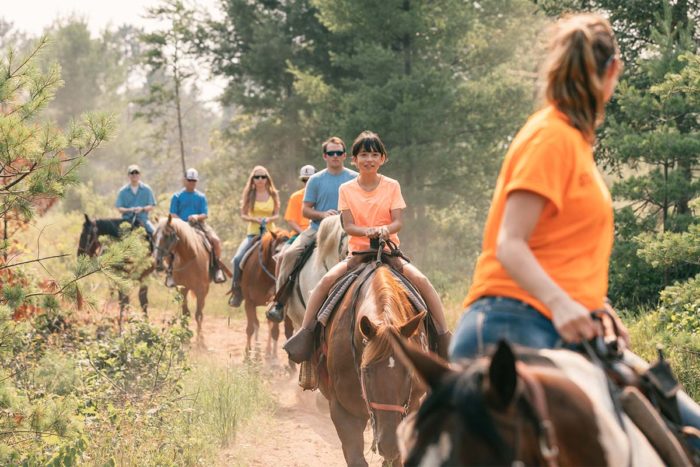 A group of people riding horses in the woods.