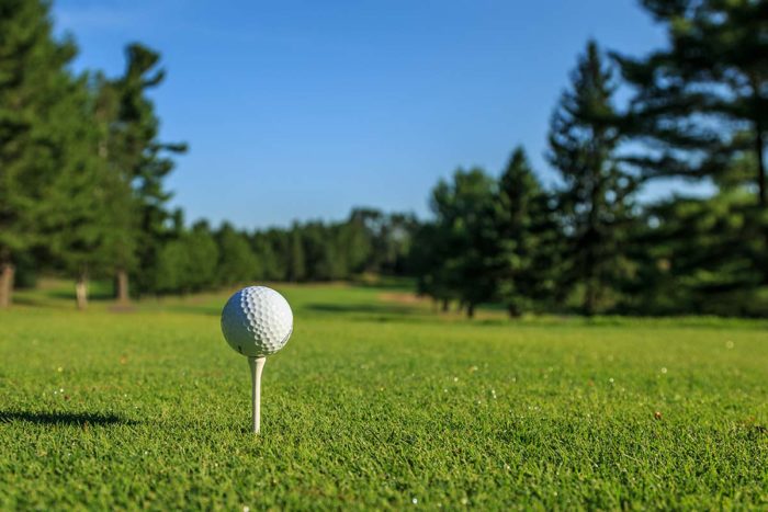 A golf ball sits on a tee in a green field.
