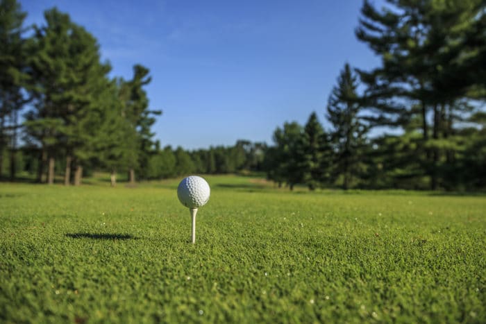 A golf ball sits on a tee in a green field.