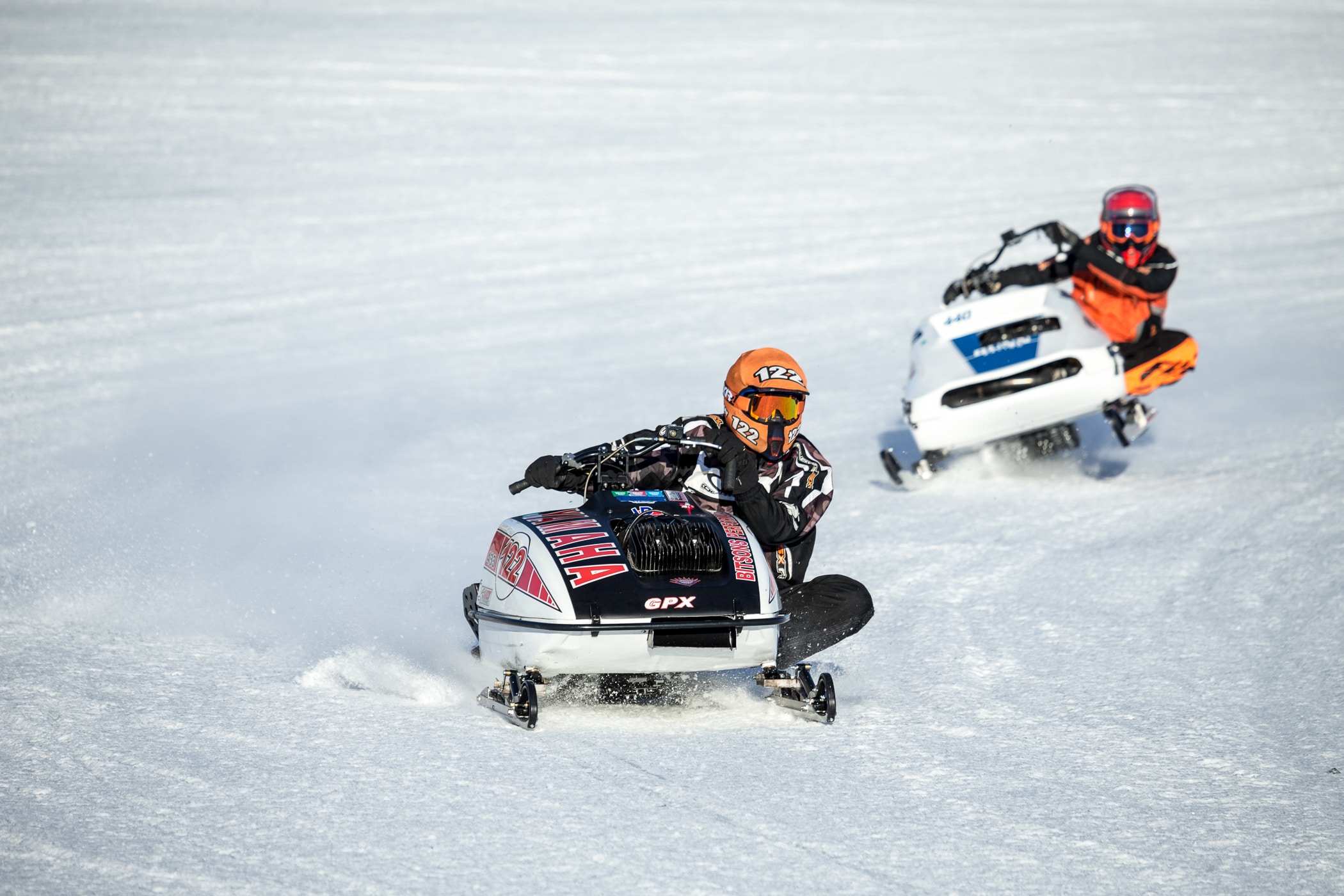 Two people riding snowmobiles on a snow covered field.