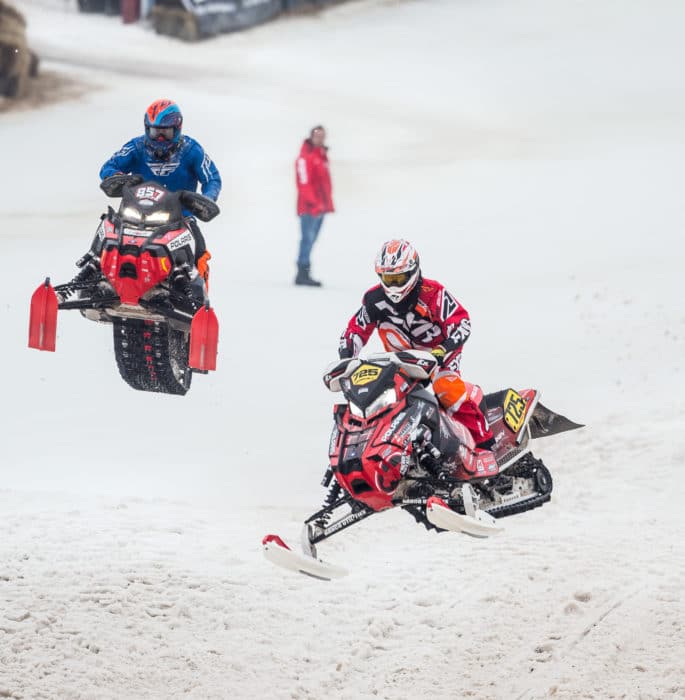 Two people riding snowmobiles in the snow.