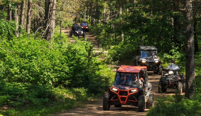 A group of people riding atvs down a trail in the woods.