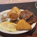 Plate with fried eggs, hash browns, bacon, baked beans, toast, and a small cup of butter.