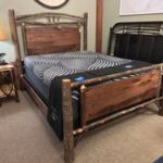 A rustic wooden bed frame with a black and gray patterned mattress is elegantly displayed in a furniture store showroom setting.