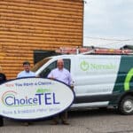 Three people stand in front of a van holding a large sign that reads "ChoiceTEL Phone & Broadband Internet Services" and "Norvado Internet TV Phone". The van has a ladder on top.