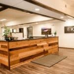 Reception area of an insurance office featuring a wooden front desk, indoor plants, wall art, and a sign reading "Klinner Insurance" welcoming clients to discuss their insurance needs.