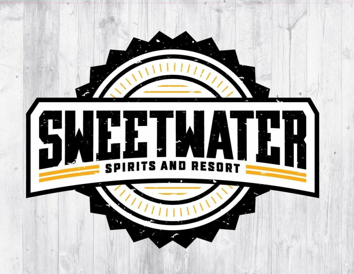 Logo of Sweetwater Spirits and Resort featuring stylized text within a circular black and yellow emblem on a wooden backdrop.