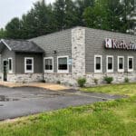 A single-story office building with a sign reading "KerberRose" on its exterior. The building, likely an accounting firm, has green siding with stone accents and is surrounded by a parking lot and grassy area.