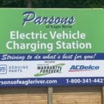 Sign for Parsons of Eagle River Electric Vehicle Charging Station, proudly featured at our dealership. Includes logos for GM Genuine Parts and AC Delco and mentions “Home of the Warranty Forever.” Contact info at bottom.