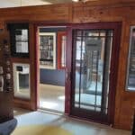 Display of sliding patio doors and windows in a Building Supply showroom, featuring a door labeled "Marvin," set against wooden walls with various product samples.