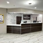 Modern motel reception desk featuring stone wall decor, wood accents, and the AmericInn logo, with posters and warm lighting.