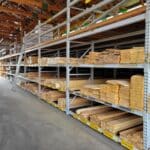 A warehouse aisle with metal shelves stacked with various sizes and types of wooden boards, perfect for any building supply needs. A metal ladder is placed against one of the shelves.