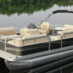 A pontoon boat with beige seating and a black canopy floats on a calm lake, reflecting the trees along the shoreline—an ideal scene for relaxing or enjoying a boat rental adventure.