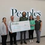 Five people posing with a large ceremonial check for $1,000 in front of a "Peoples State Bank" sign.