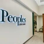 Interior view of Peoples State Bank with its sign proudly displayed on a wall. The space is well-lit, boasting a modern design that elegantly blends stone and wooden elements.