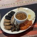 Full English breakfast with baked beans, sausages, black pudding, mushrooms, grilled tomatoes, fried egg, and toasted bread on a white plate.