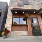 Front view of a stone and wood exterior building with a sign reading "Toad in the Hole." This charming restaurant features a large window, a dark door with a notice, and potted plants adding to its inviting atmosphere.