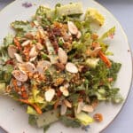 A restaurant-ready plate of leafy green salad topped with sliced almonds, grated cheese, croutons, and a variety of seeds.