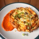 A restaurant-worthy plate featuring a cheesy omelette garnished with green onions, accompanied by a dollop of red sauce on the side.