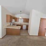 Kitchen with wooden cabinets, white appliances, and beige tile flooring. Adjacent is a carpeted room with a wooden door and sloped ceiling.