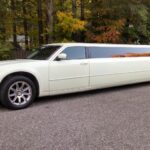 A white chrysler limo is parked on the side of the road.