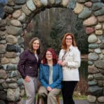 Three women posing for a photo under a stone archway outdoors.
