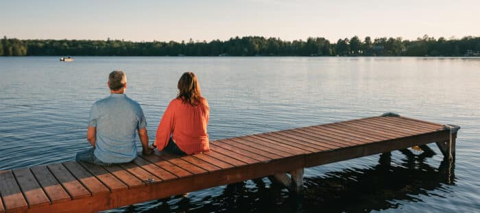 Two people sitting on a wooden dock overlooking a serene lake during sunset.