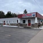 A single-story re/max property pros office building with a red and white sign, stone accents, and a parking lot.