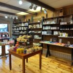 A store interior with wooden shelves and tables displaying a variety of colorful soaps, lotions, and bath products. Wooden floor and walls create a rustic atmosphere.