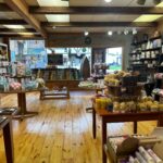 A wooden-floored store stocked with various bath and body products including soaps, sponges, candles, and bath bombs, displayed on tables and shelves.