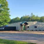 Industrial building with a sign reading "iconik" under a clear blue sky, surrounded by greenery and a gravel driveway.