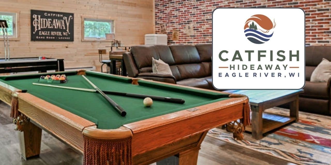 A recreation room with a pool table, cue sticks, a brown sectional sofa, and a sign reading "Catfish Hideaway Eagle River, WI.