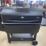 A large black pellet grill on wheels with a front display and logo in a store setting.