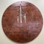 Circular wooden sign with carved trees and the text "Everything I Love Boutique.