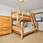 Wooden bunk bed with a ladder, next to a matching wooden dresser, in a carpeted bedroom with a window.