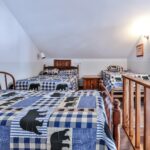 Loft bedroom with three single beds featuring bear-themed quilts, a wooden chair, wooden railing, and a sloped ceiling.